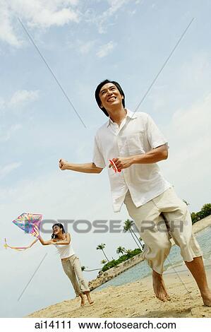 Stock Image - Couple flying kite along beach. Fotosearch