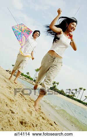 Couple flying kite along beach, woman running in front of man View Large Photo Image Picture - Couple flying kite along beach, woman running in front of man. Fotosearch