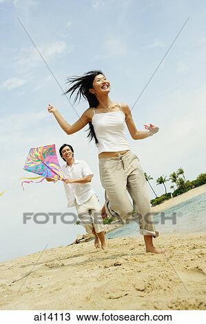 Couple flying kite along beach, woman running in front of man View Large Photo Image Stock Image - Couple flying kite along beach, woman running in front of man. Fotosearch