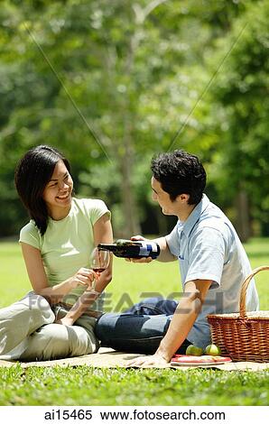 Stock Photography - Couple having picnic in park, man pouring wine for woman. Fotosearch