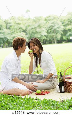 Couple having picnic in park, woman eating apple View Large Photo Image Stock Photo - Couple having picnic in park, woman eating apple. Fotosearch
