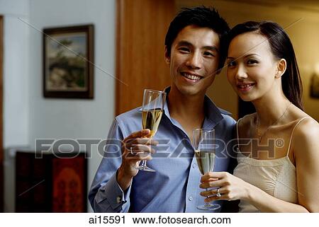 Stock Image - Couple holding champagne glasses, smiling at camera. Fotosearch
