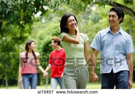 Couple holding hands and walking in park, people in the background View Large Photo Image Stock Photo - Couple holding hands and walking in park, people in the background. Fotosearch