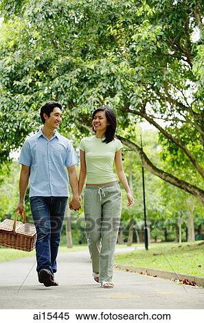 Stock Photography - Couple holding hands and walking, man carrying picnic basket. Fotosearch