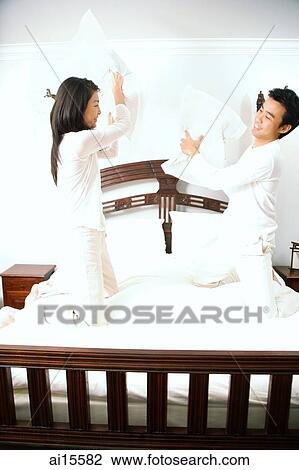 Stock Image - Couple holding pillows, fighting. Fotosearch