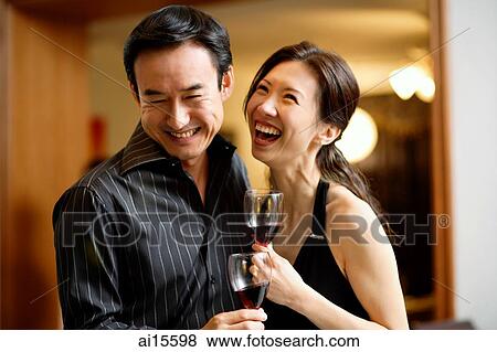 Stock Photo - Couple holding wine glasses, laughing. Fotosearch