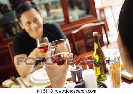 Couple holding wine glasses, sitting opposite each other View Large Photo Image Stock Photo - Couple holding wine glasses, sitting opposite each other. Fotosearch