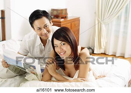Stock Image - Couple in bedroom, lying on bed, looking at camera. Fotosearch