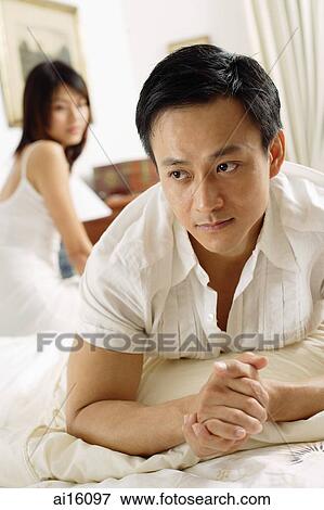 Couple in bedroom, man lying down, looking away, woman sitting behind him View Large Photo Image Stock Photo - Couple in bedroom, man lying down, looking away, woman sitting behind him. Fotosearch