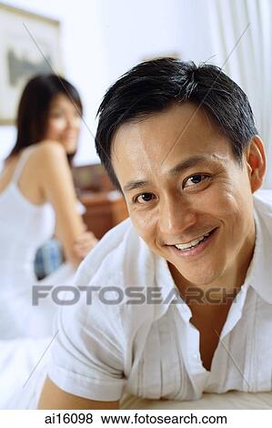 Couple in bedroom, man lying down, looking at camera, woman sitting behind him View Large Photo Image Stock Photo - Couple in bedroom, man lying down, looking at camera, woman sitting behind him. Fotosearch