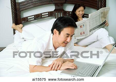 Couple in bedroom, man using laptop, woman reading newspaper View Large Photo Image Stock Photography - Couple in bedroom, man using laptop, woman reading newspaper. Fotosearch