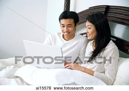 Stock Photo - Couple in bedroom, using laptop. Fotosearch
