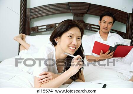 Couple in bedroom, woman holding pen, man reading book View Large Photo Image Picture - Couple in bedroom, woman holding pen, man reading book. Fotosearch