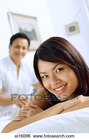 Couple in bedroom, woman lying down, smiling at camera, man sitting behind her View Large Photo Image Stock Photograph - Couple in bedroom, woman lying down, smiling at camera, man sitting behind her. Fotosearch