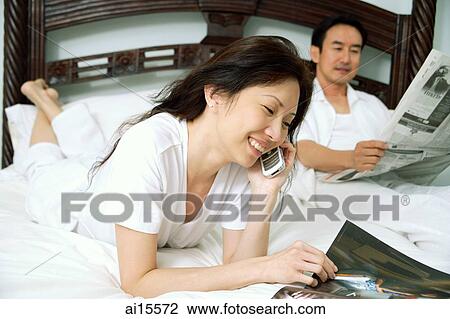 Couple in bedroom, woman reading magazine and using mobile phone, man reading newspaper View Large Photo Image Stock Image - Couple in bedroom, woman reading magazine and using mobile phone, man reading newspaper. Fotosearch