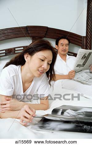 Couple in bedroom, woman reading magazine, man reading newspaper View Large Photo Image Stock Photo - Couple in bedroom, woman reading magazine, man reading newspaper. Fotosearch