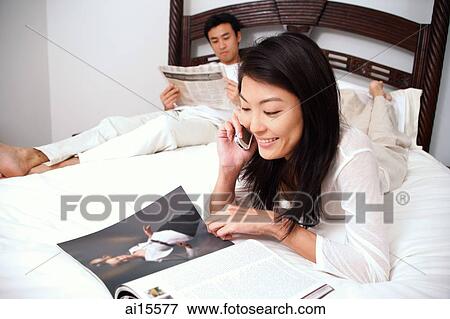 Couple in bedroom, woman reading magazine and using mobile phone, man reading newspaper View Large Photo Image Stock Photo - Couple in bedroom, woman reading magazine and using mobile phone, man reading newspaper. Fotosearch