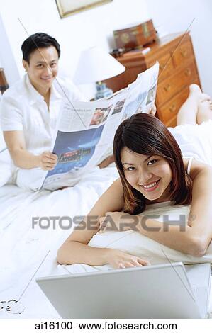 Couple in bedroom, woman with laptop, man sitting behind her reading newspaper View Large Photo Image Stock Image - Couple in bedroom, woman with laptop, man sitting behind her reading newspaper. Fotosearch
