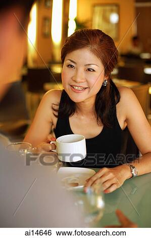 Stock Photograph - Couple in cafe, woman holding cup, looking at man across from her. Fotosearch