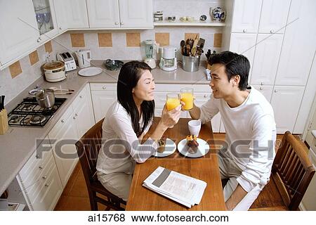 Couple in kitchen, having breakfast, holding glasses of orange juice View Large Photo Image Stock Photo - Couple in kitchen, having breakfast, holding glasses of orange juice. Fotosearch