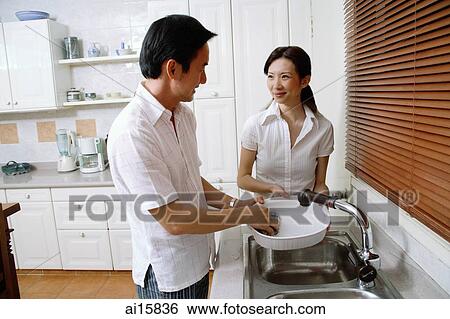 Couple in kitchen, man washing dishes, woman next to him View Large Photo Image Stock Photograph - Couple in kitchen, man washing dishes, woman next to him. Fotosearch