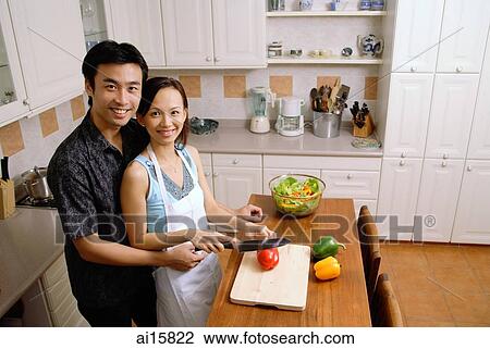 Couple in kitchen, woman cutting vegetables, smiling up at camera View Large Photo Image Stock Image - Couple in kitchen, woman cutting vegetables, smiling up at camera. Fotosearch