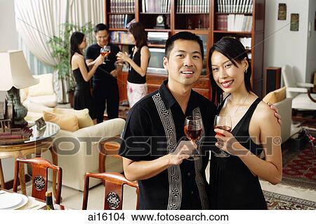 Couple in living room, holding wine glasses, smiling at camera View Large Photo Image Picture - Couple in living room, holding wine glasses, smiling at camera. Fotosearch