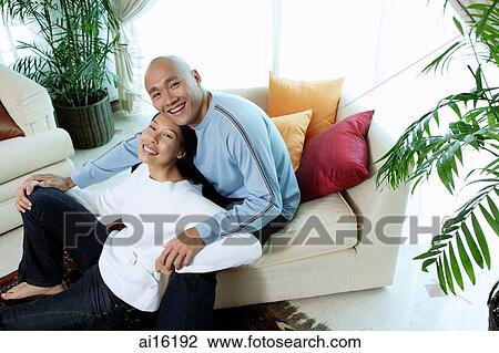 Stock Image - Couple in living room, looking up at camera. Fotosearch