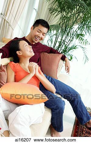 Couple in living room, sitting on sofa, woman with hands clasped View Large Photo Image Stock Photo - Couple in living room, sitting on sofa, woman with hands clasped. Fotosearch