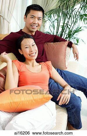Couple in living room, sitting on sofa, smiling at camera, portrait View Large Photo Image Stock Photograph - Couple in living room, sitting on sofa, smiling at camera, portrait. Fotosearch