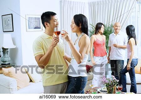 Couple in living room, toasting with wine glasses, people in the background View Large Photo Image Stock Photo - Couple in living room, toasting with wine glasses, people in the background. Fotosearch
