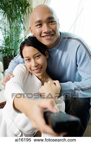 Stock Photography - Couple in living room, woman holding remote control forward. Fotosearch