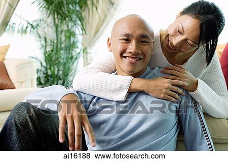 Stock Photo - Couple in living room, woman with arm around man, man smiling at camera. Fotosearch