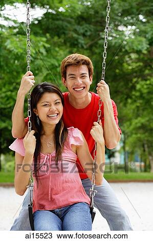 Couple in playground, woman sitting on swing, man behind her, looking at camera View Large Photo Image Stock Image - Couple in playground, woman sitting on swing, man behind her, looking at camera. Fotosearch