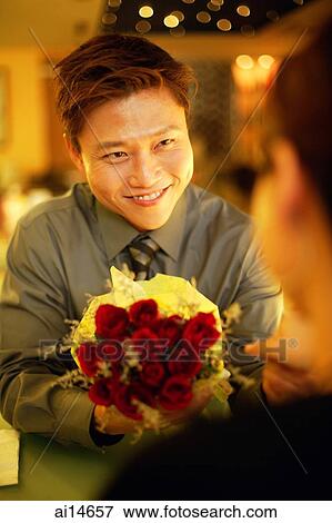 Couple in restaurant, man holding out floral bouquet to woman View Large Photo Image Stock Photo - Couple in restaurant, man holding out floral bouquet to woman. Fotosearch