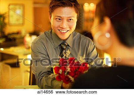 Couple in restaurant, man holding out bouquet to woman View Large Photo Image Stock Photograph - Couple in restaurant, man holding out bouquet to woman. Fotosearch