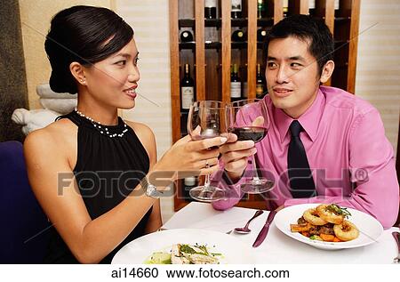 Stock Image - Couple in restaurant raising wine glasses for a toast. Fotosearch