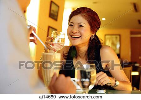 Stock Image - Couple in restaurant, woman holding glass and smiling. Fotosearch