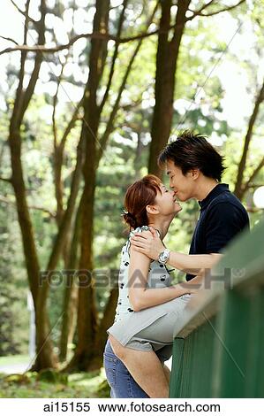 Stock Photography - Couple kissing, man sitting on railing, woman standing next to him. Fotosearch