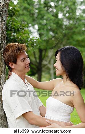 Couple leaning on tree, embracing, looking at each other View Large Photo Image Stock Photo - Couple leaning on tree, embracing, looking at each other. Fotosearch