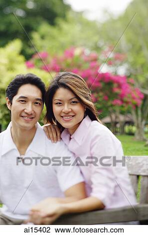 Stock Image - Couple looking at camera, sitting side by side. Fotosearch