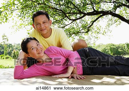 Couple looking at camera, woman lying down, man sitting behind her View Large Photo Image Stock Image - Couple looking at camera, woman lying down, man sitting behind her. Fotosearch