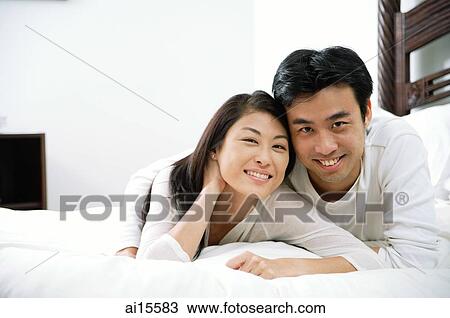 Stock Image - Couple lying in bed, looking at camera. Fotosearch