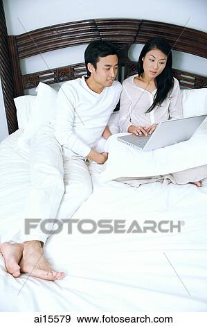 Couple lying in bed, using laptop View Large Photo Image Stock Photo - Couple lying in bed, using laptop. Fotosearch