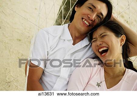 Stock Image - Couple lying in hammock on beach, laughing. Fotosearch