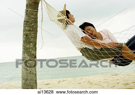 Stock Photo - Couple lying in hammock on beach, sleeping. Fotosearch