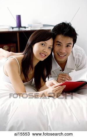 Couple lying on bed, holding book, looking at camera View Large Photo Image Stock Image - Couple lying on bed, holding book, looking at camera. Fotosearch