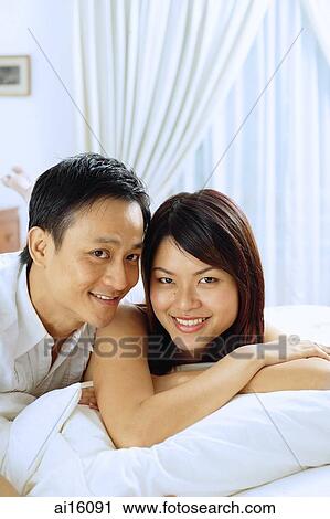 Couple lying on bed, looking at camera View Large Photo Image Stock Image - Couple lying on bed, looking at camera. Fotosearch