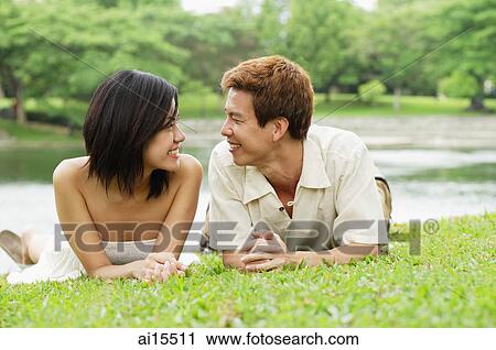 Stock Image - Couple lying on grass, smiling at each other. Fotosearch