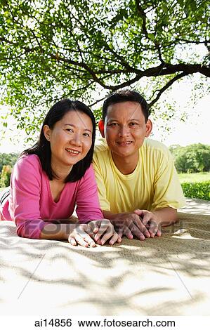 Couple lying on picnic mat, looking at camera View Large Photo Image Stock Photograph - Couple lying on picnic mat, looking at camera. Fotosearch